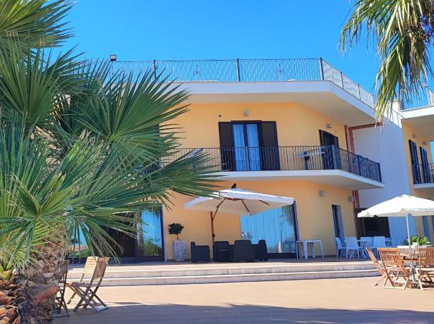 Edificio giallo con palme e terrazza, cielo azzurro.