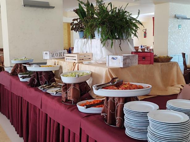 Buffet con piatti, verdure e pane in una sala da pranzo elegante.