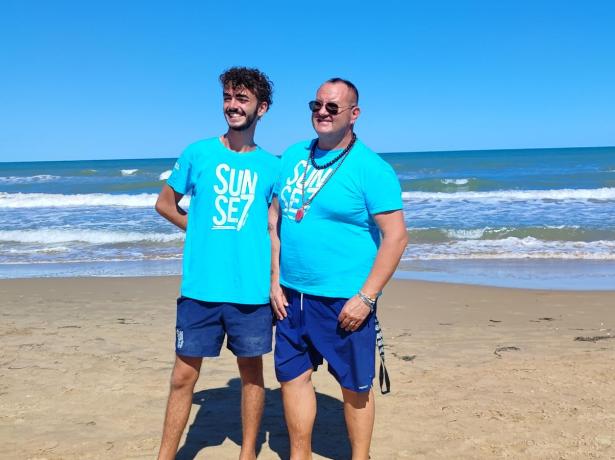 Due uomini in spiaggia con magliette blu.