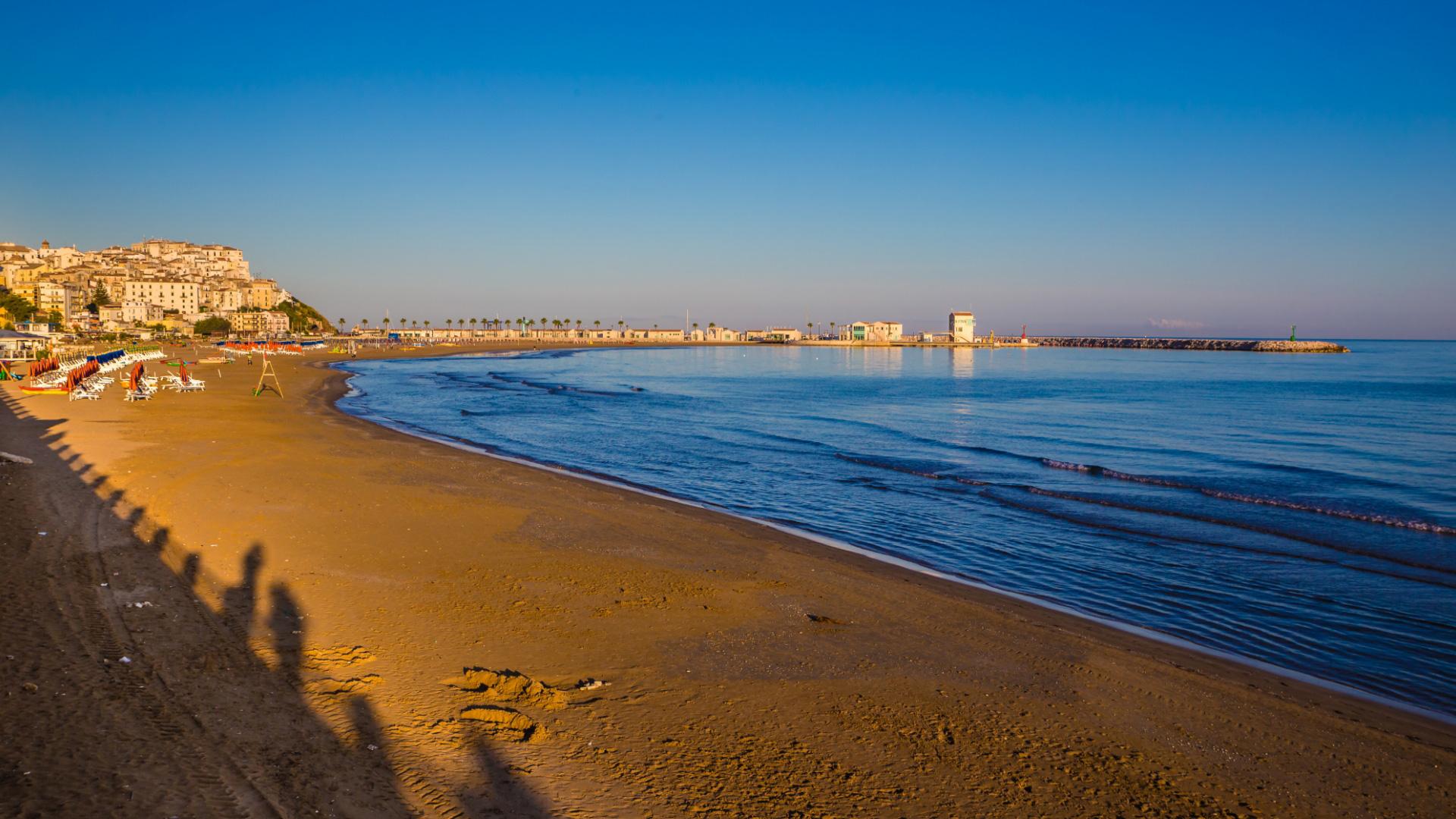 Spiaggia al tramonto con ombrelloni e vista su una città costiera.