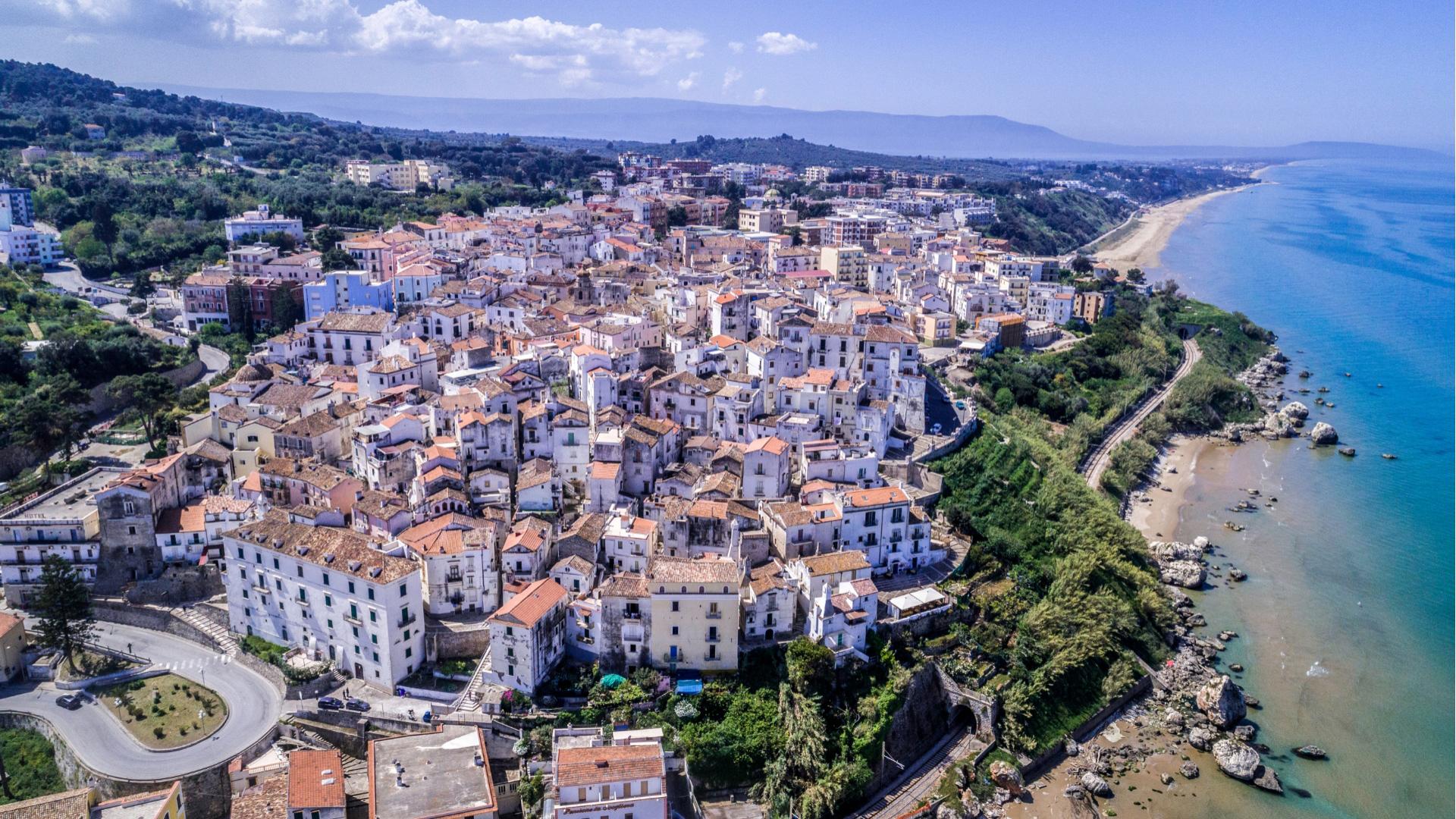 Panorama di una città costiera con case storiche e una lunga spiaggia sabbiosa.