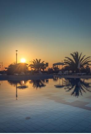 Tramonto riflesso in una piscina con palme e cielo sereno.