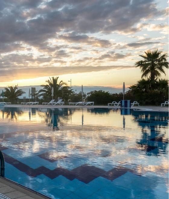 Piscina all'aperto al tramonto, con lettini e palme sullo sfondo.