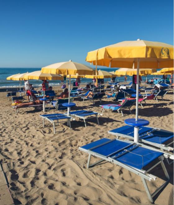 Spiaggia affollata con ombrelloni gialli e lettini blu sotto un cielo sereno.