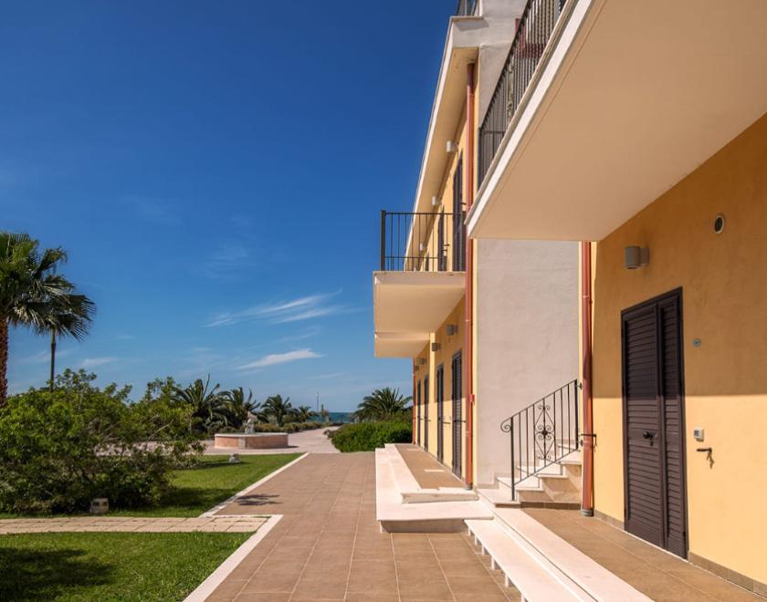 Edificio moderno con balconi, giardino curato e vista sul mare, sotto un cielo sereno.